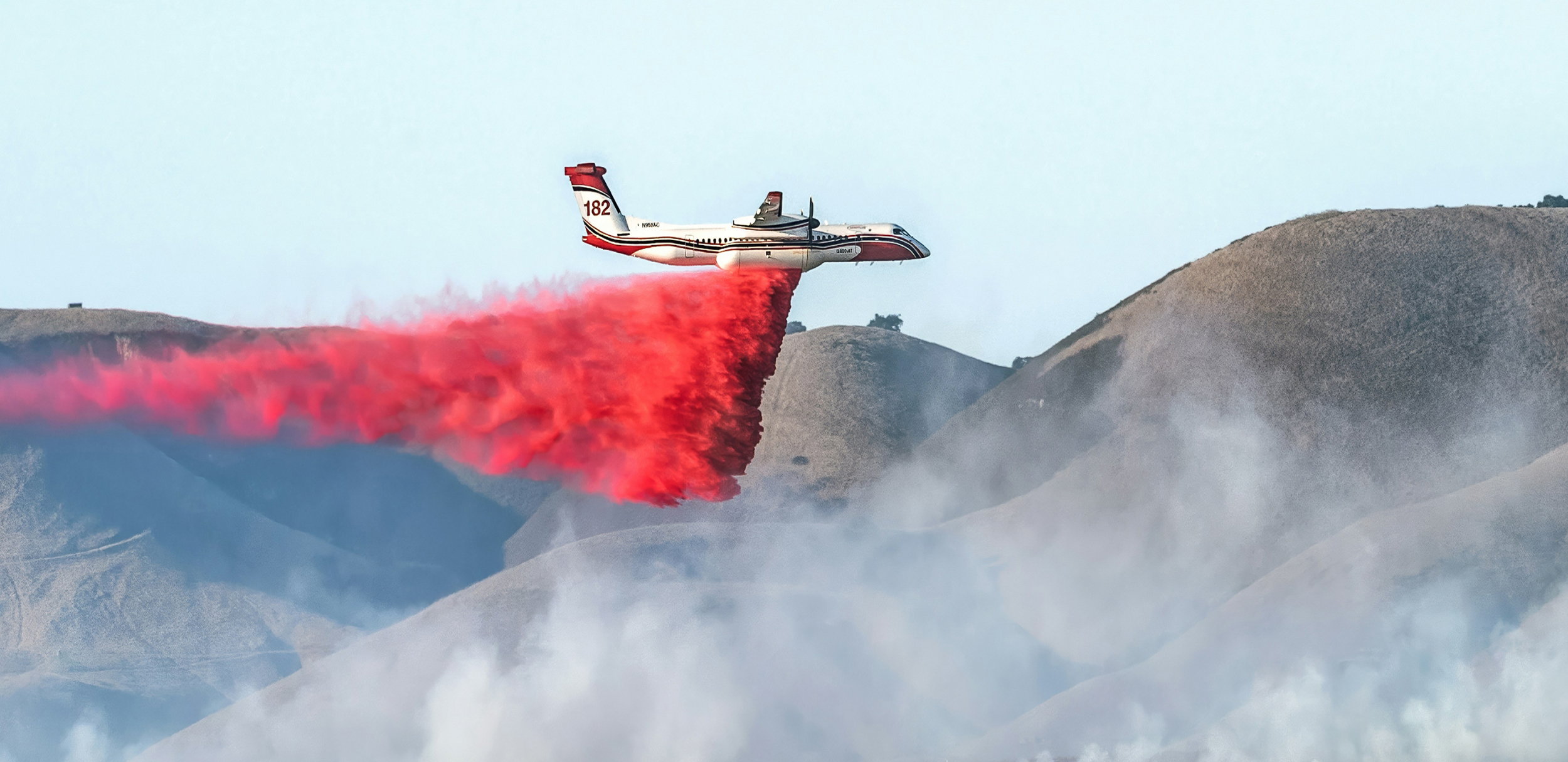 Plane dropping flame retardant over smoky hills